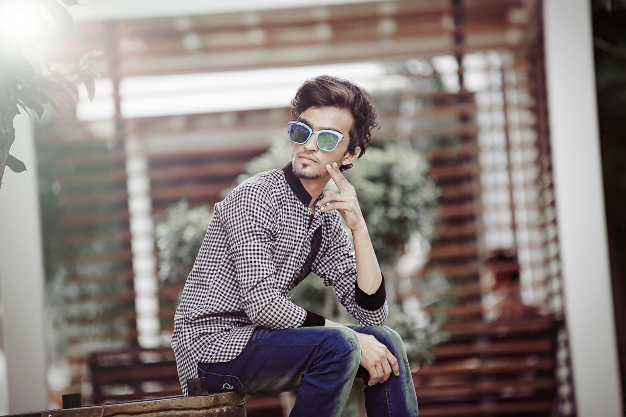 faq-img Stylish young man in sunglasses posing confidently in an outdoor urban environment.