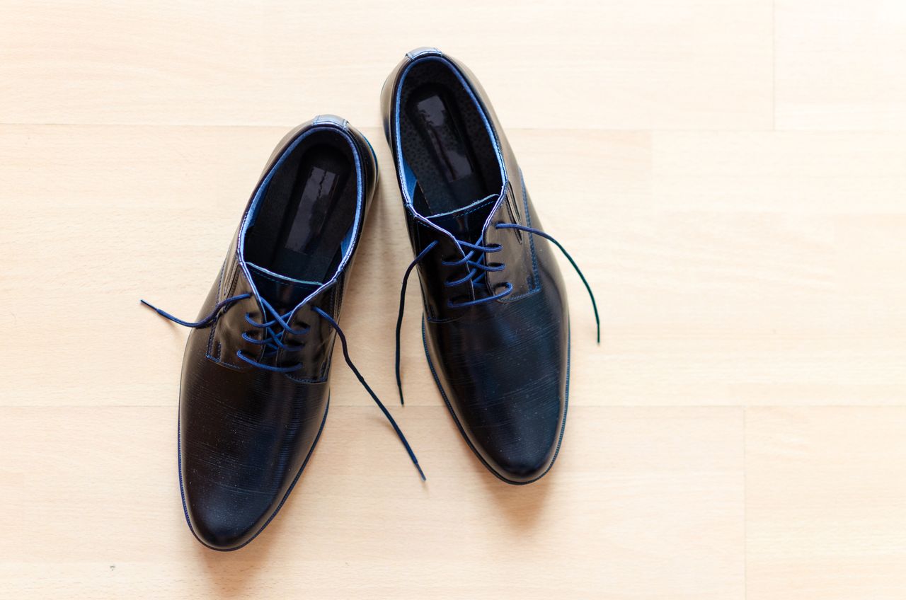 collection-04 Pair of stylish black leather shoes with blue laces on a wooden floor.