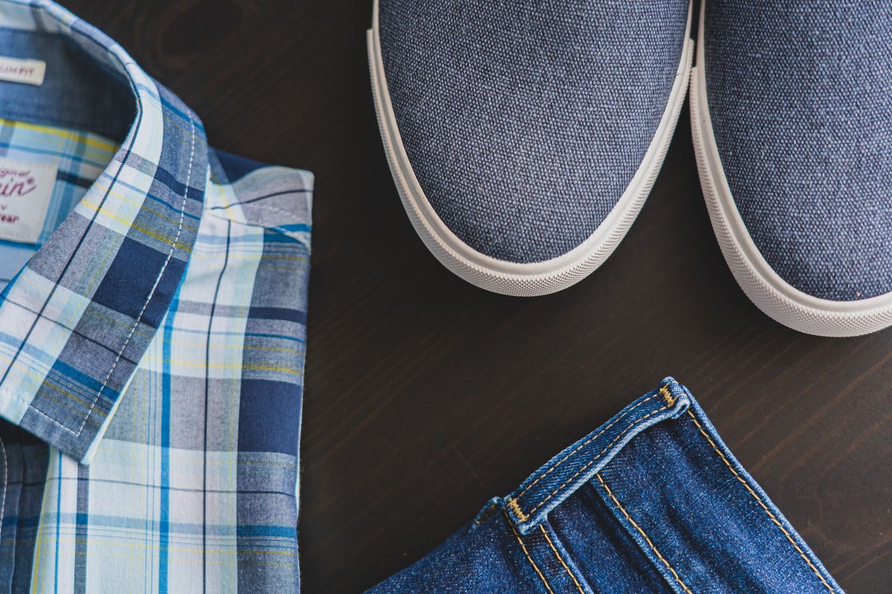 hero-img Flat lay of a casual men's outfit with checkered shirt, denim jeans, and blue sneakers.
