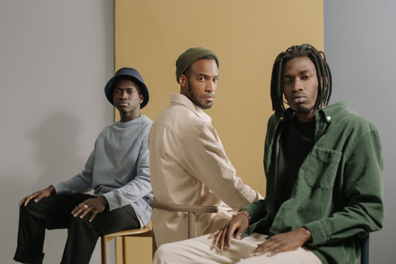 collection-05 Three stylish men sitting in a minimalist studio with neutral tones and fashionable outfits.