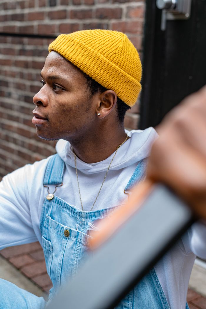 summer-sale Stylish young man wearing denim overalls and a yellow beanie in an urban setting.