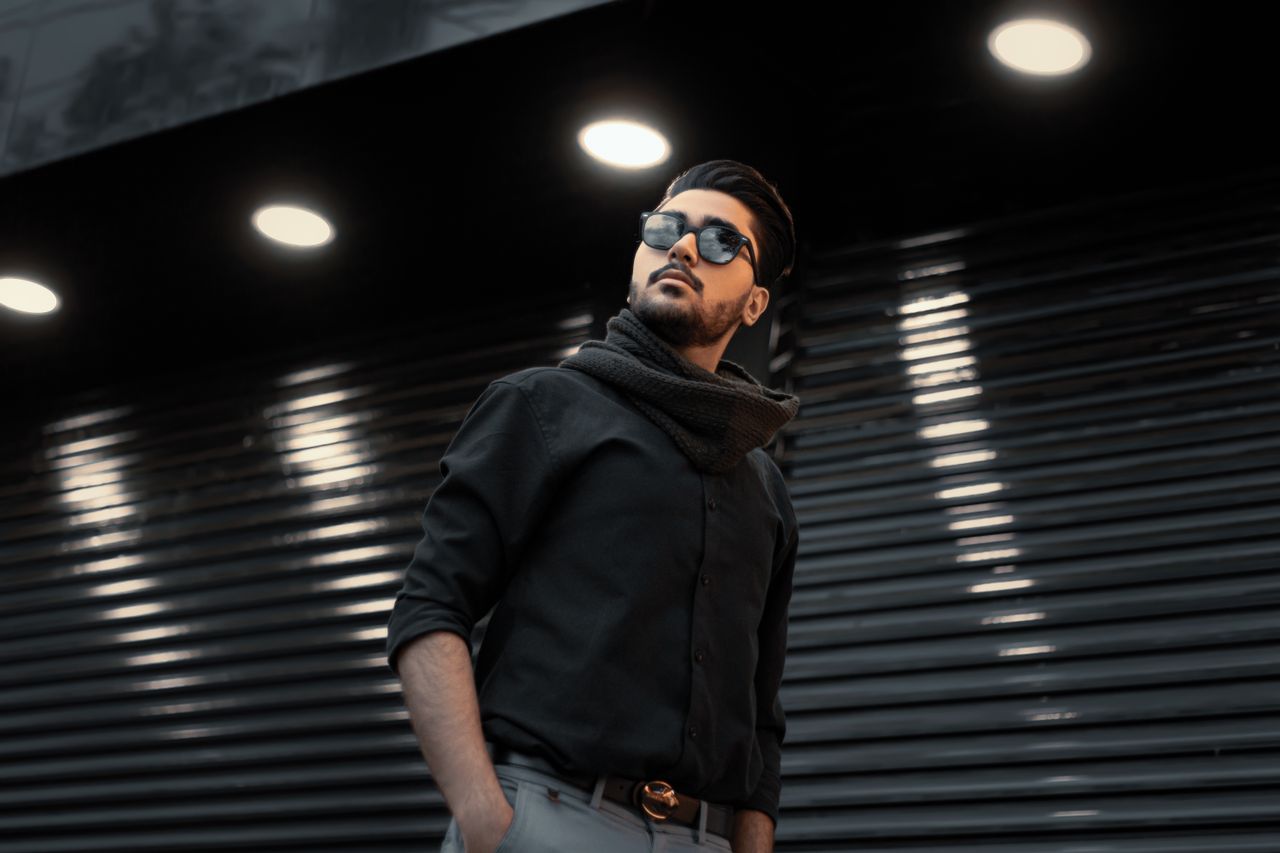 The Art of Drawing Readers In: Your attractive post title goes here A fashionable man in sunglasses with a scarf poses under spotlights in an urban setting.
